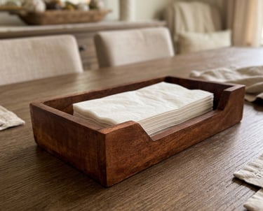 Handcrafted wooden napkin holder with white paper napkins on a rustic oak dining table.